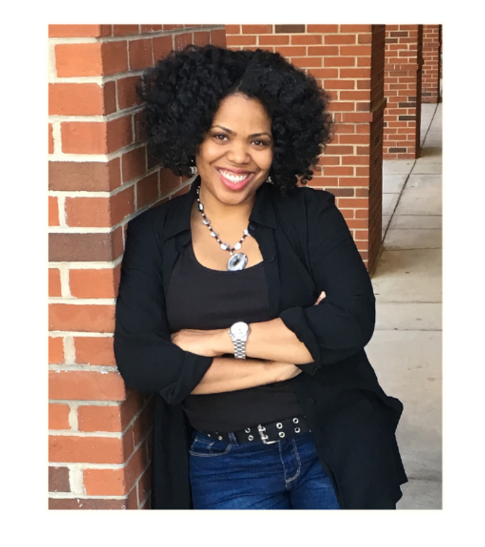 Tiffany Elder smiling, standing beside a brick wall